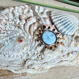 Feine Halskette aus rhodiniertem 925 Silber mit Sonnen-Anhänger und rundem Larimar-Cabochon, 10 mm. Der seltene, hellblaue Stein aus der Dominikanischen Republik erinnert an Meer und Himmel. Gesamtgröße des Anhängers ca. 20 x 19 mm, Ankerkette 45 cm, ca. 1 mm stark. Edler, maritimer Schmuck, geliefert in einer Geschenkbox.