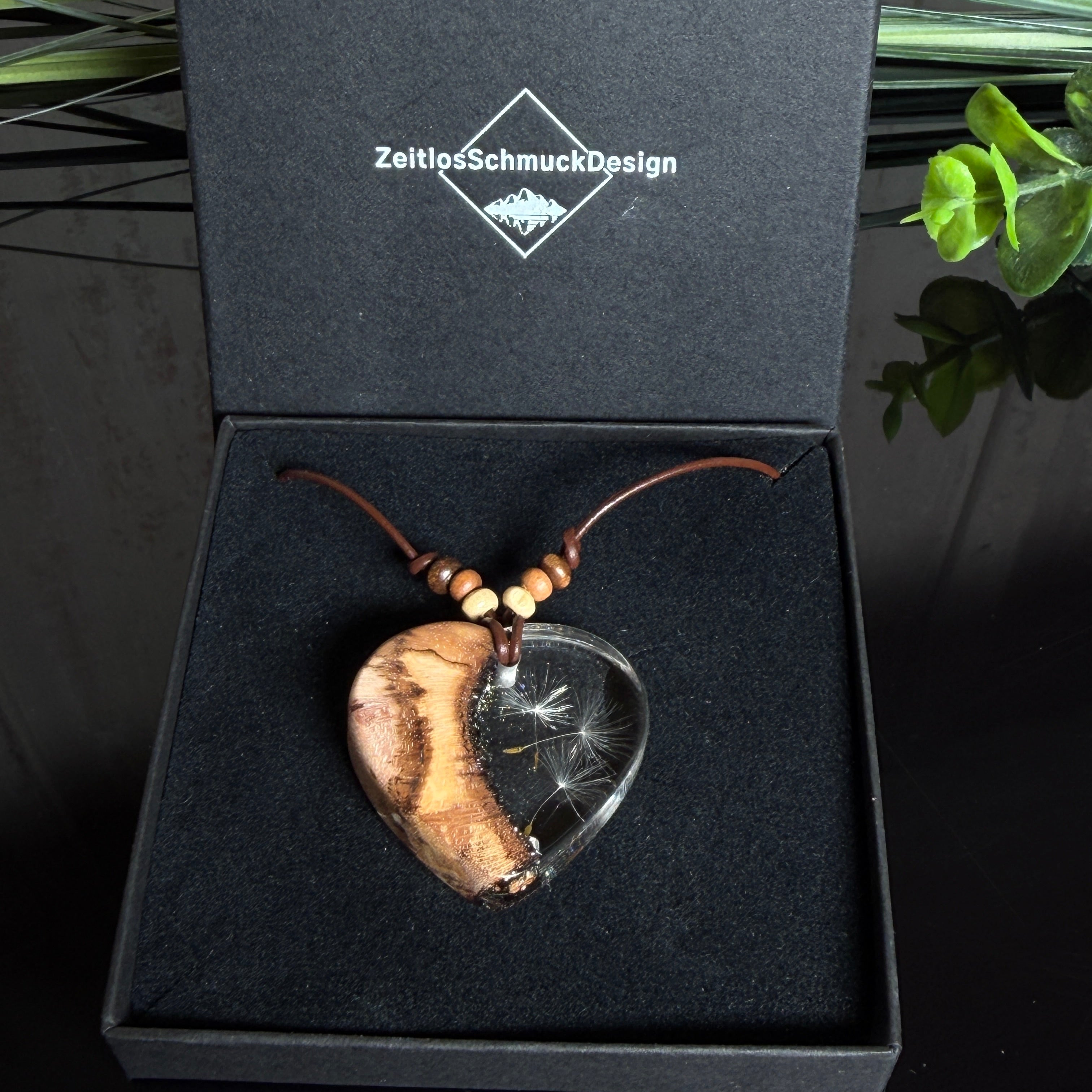 Herzanhänger „Pusteblumenzauber“ aus naturbelassenem Rebholz und klarem Epoxidharz mit schwebenden Pusteblumensamen. Dunkelbraunes, verstellbares Lederband mit kleinen Holzperlen, Anhänger ca. 3,5 × 3,5 cm. Handgefertigtes Unikat von ZeitlosSchmuckDesign.