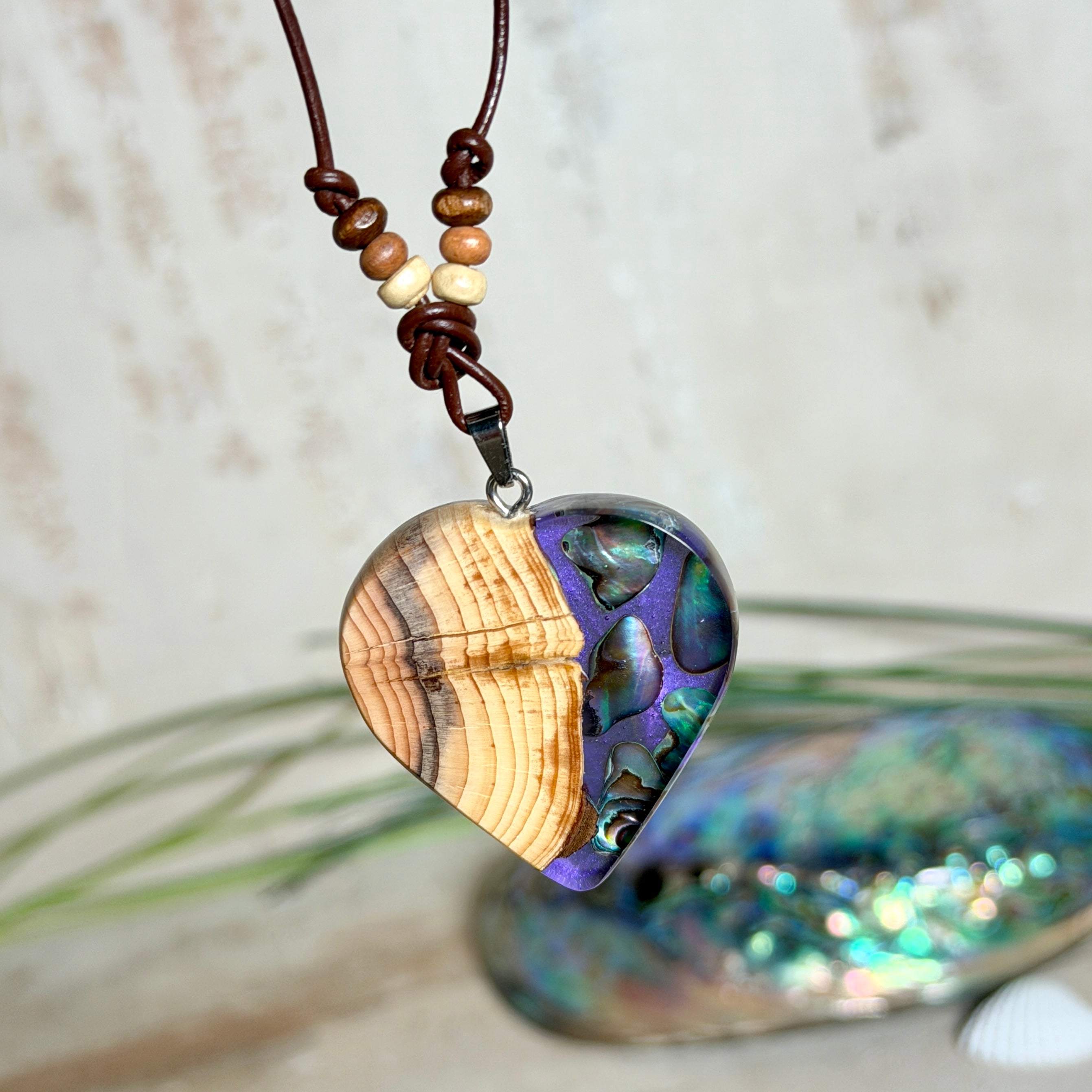Handgemachter Herzanhänger aus Eibenholz mit lila Harz und Paua-Muschel-Inlay an braunem, verstellbarem Lederband.