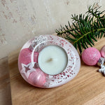 Rosa Teelichthalter aus klarem Epoxidharz, ca. 8 × 6,5 cm, Höhe ca. 4 cm. Im Harz sind kleine rosa Weihnachtskugeln, ein Stern, eine Schneeflocke und rosa Granulat eingegossen. Ovaler Halter für ein Teelicht, Unterseite mit vier runden Korkpads als Möbelschoner. Fotografiert auf Holz mit Tannenzweig und rosa Kugeln als weihnachtlicher Dekohintergrund.