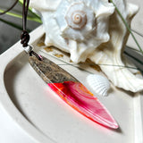 Aurora Flame – fluoreszierender Surfbrett-Anhänger aus Maserholz und leuchtendem Epoxidharz in Rosa, Pink, Orange und Weiß. Der handgefertigte Unikat-Anhänger fluoresziert bei Schwarzlicht in intensiven Farbtönen. Er ist ca. 6,3 x 2 cm groß, wird an einem verstellbaren Lederband (26–45 cm) getragen und ist mit einer silberfarbenen Spacerperle verziert. Ein ausdrucksstarkes Schmuckstück für Menschen mit Persönlichkeit.