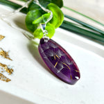 Ovaler Anhänger mit echter Pusteblume in Harz, Hintergrund Brombeerfarben. Größe 4 × 1,8 cm, versilberte Kette 50 cm mit Karabinerverschluss. Handgefertigtes Unikat.