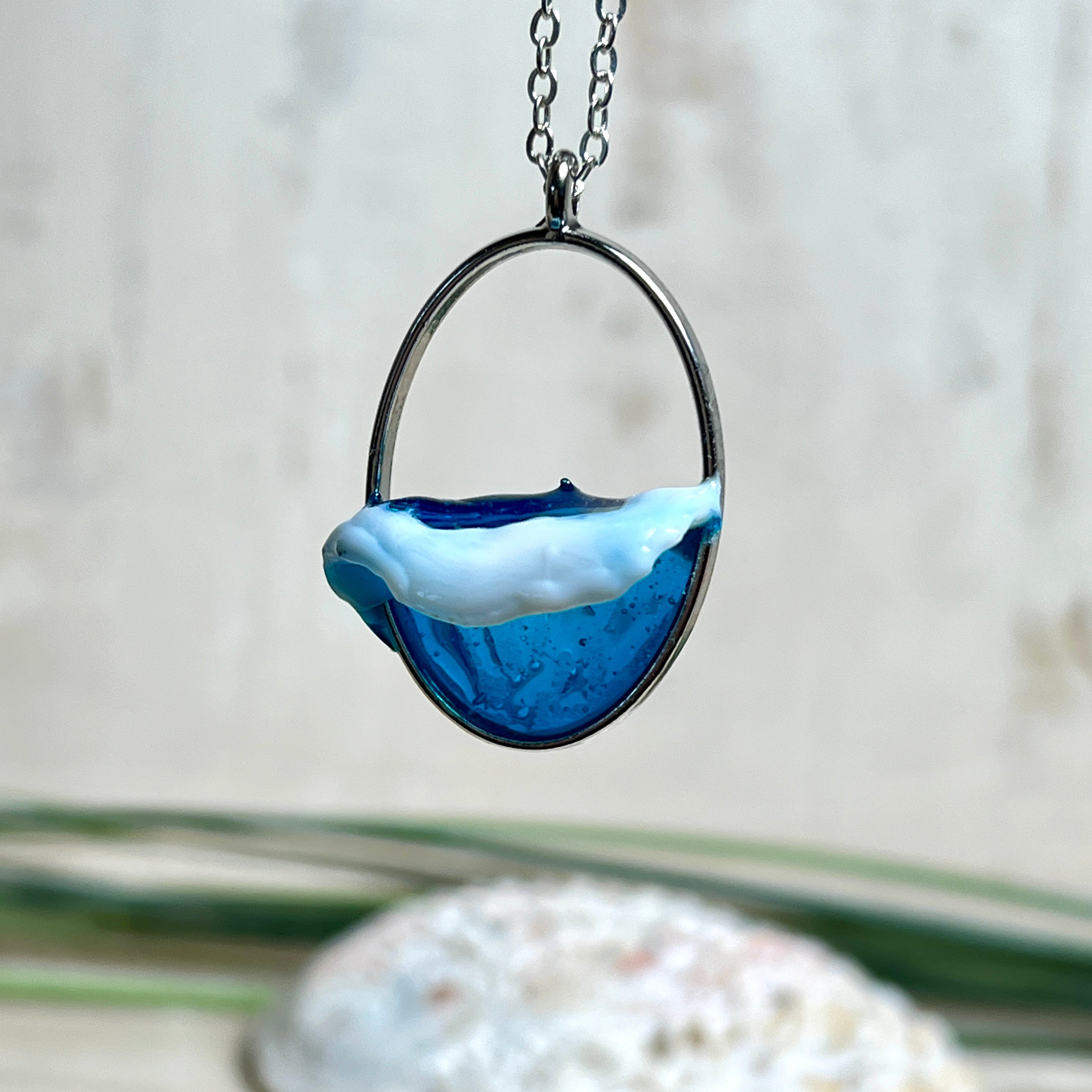 Ovale Halskette „Ocean Crest“ mit 3D-Welle: handgefertigter Harz-Anhänger in Silber-Legierung, Farbverlauf von Tiefblau zu Türkis mit weißer Schaumkrone. Größe ca. 3,9 × 2,3 cm, an einer ca. 56 cm langen versilberten Kette. Glänzende Oberfläche, maritimer Look, Unikat-Handarbeit.