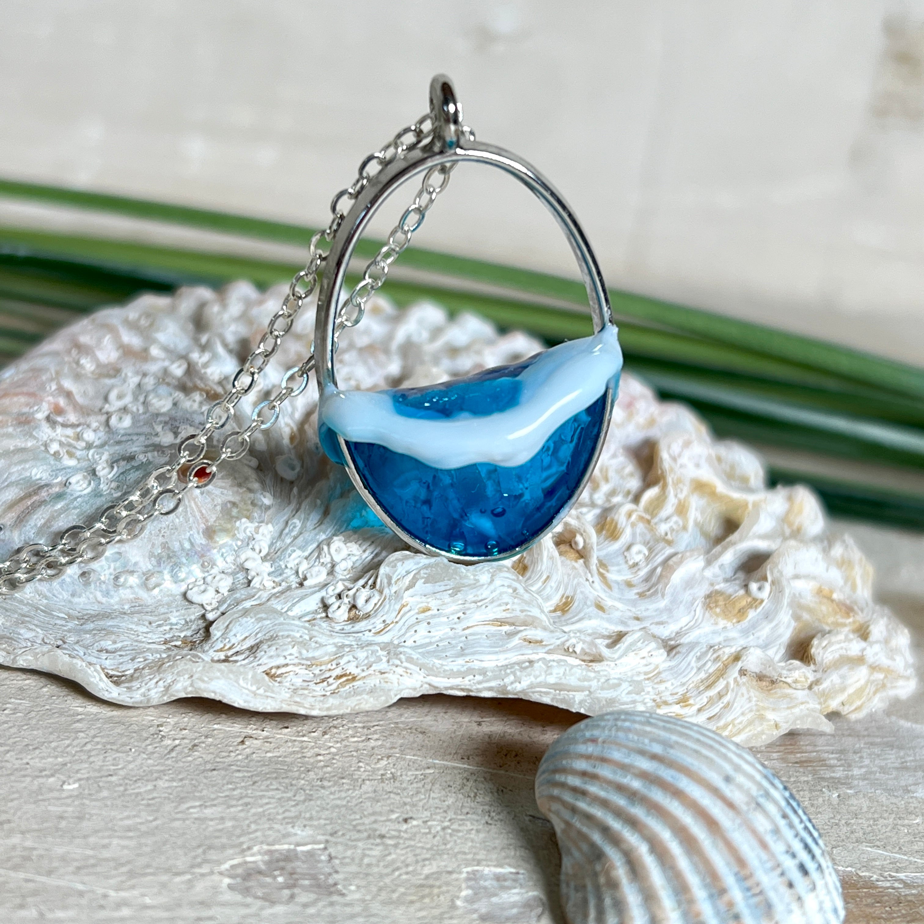 Ovale Halskette „Ocean Crest“ mit 3D-Welle: handgefertigter Harz-Anhänger in Silber-Legierung, Farbverlauf von Tiefblau zu Türkis mit weißer Schaumkrone. Größe ca. 3,9 × 2,3 cm, an einer ca. 56 cm langen versilberten Kette. Glänzende Oberfläche, maritimer Look, Unikat-Handarbeit.