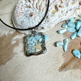 Quadratischer Larimar-Mosaik Anhänger im Edelstahlrahmen mit Seestern-Element und facettierter Bergkristall-Perle, eingebettet in Harz, an schwarzer Lederkette.