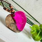 Handgefertigter Herzanhänger aus Olivenholz und leuchtend pinkem Epoxidharz mit eingeschlossenen Pusteblumensamen. Verstellbares braunes Lederband mit Holzperlen, Anhänger ca. 3,5 × 3,3 cm groß. Das Harz leuchtet dezent unter Schwarzlicht. Ein einzigartiges Unikat von ZeitlosSchmuckDesign, inspiriert von Kindheitsglück und Pusteblumen.