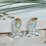 Kleiner Bärchen-Anhänger aus transparentem Harz mit irisierenden Flakes in Regenbogen-Schimmer, goldfarbene Anhängerschlaufe aus Edelstahl. Größe ca. 2,2 × 2,1 cm. Handgefertigtes Unikat; Flakes-Anordnung variiert, vereinzelt kleine Luftbläschen möglich.
