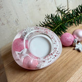 Rosa Teelichthalter aus klarem Epoxidharz, ca. 8 × 6,5 cm, Höhe ca. 4 cm. Im Harz sind kleine rosa Weihnachtskugeln, ein Stern, eine Schneeflocke und rosa Granulat eingegossen. Ovaler Halter für ein Teelicht, Unterseite mit vier runden Korkpads als Möbelschoner. Fotografiert auf Holz mit Tannenzweig und rosa Kugeln als weihnachtlicher Dekohintergrund.