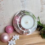 Runder Teelichthalter aus klarem Epoxidharz, Durchmesser ca. 7 cm, Höhe ca. 4 cm. Im Harz sind rosa Weihnachtskugeln, ein Stern, eine Schneeflocke, ein Tannenbaum, künstliche Tannennadeln und feiner Glitzer eingegossen. Vertiefung für ein Teelicht in der Mitte, Unterseite mit vier Korkpads als Möbelschoner. Fotografiert auf Holz mit Tannenzweig und rosa Kugeln als weihnachtliche Dekoration