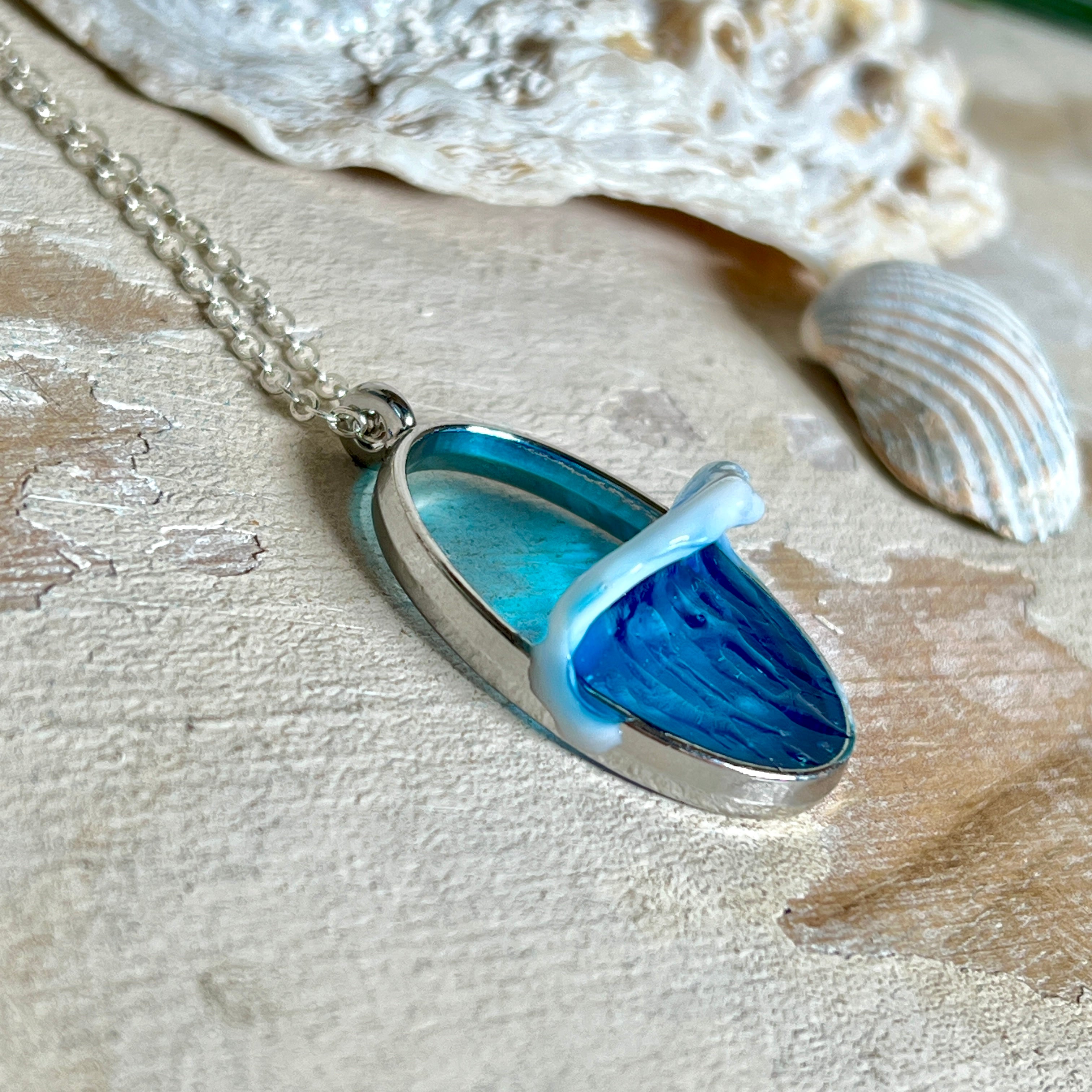 Ovale Halskette „Ocean Crest“ mit 3D-Welle: handgefertigter Harz-Anhänger in Silber-Legierung, Farbverlauf von Tiefblau zu Türkis mit weißer Schaumkrone. Größe ca. 3,9 × 2,3 cm, an einer ca. 56 cm langen versilberten Kette. Glänzende Oberfläche, maritimer Look, Unikat-Handarbeit.