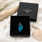 WELLENKAMM Anhänger aus Maserholz und blau-türkisem Epoxidharz mit weißer Gischtoptik, präsentiert in der Schmuckbox von ZeitlosSchmuckDesign – handgefertigter maritimer Naturschmuck am verstellbaren Lederband, einzigartiges Unikat für Meeresliebhaber und Strandfans.