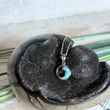 Feine Wellen-Kette aus rhodiniertem 925 Silber. Der runde Anhänger zeigt eine stilisierte Welle mit hellblauem Larimar-Cabochon, eingefasst in poliertem Silber. Größe des Anhängers ca. 23 x 13 mm, an einer 45 cm langen, 1 mm starken, rhodinierten Silberkette. 