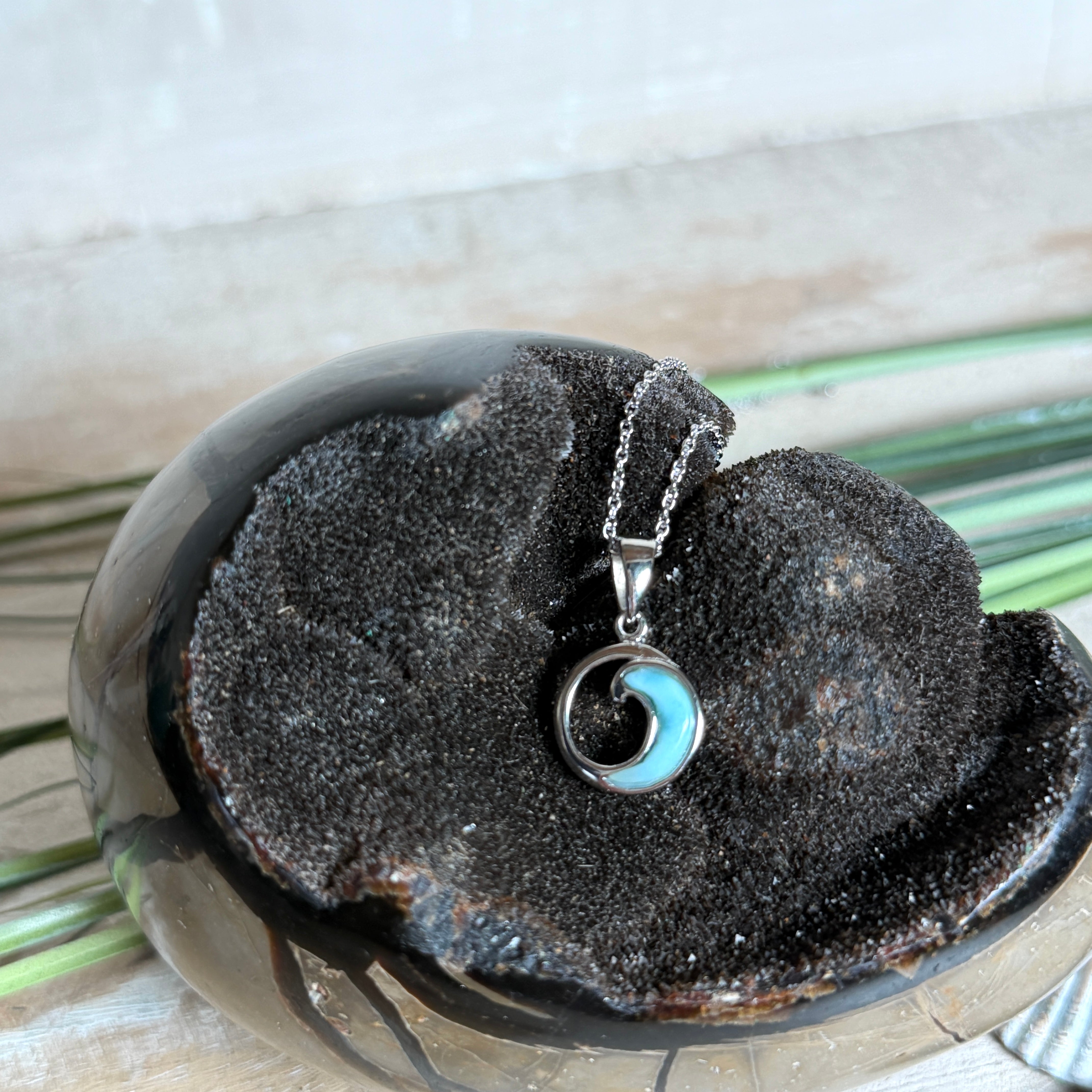 Feine Wellen-Kette aus rhodiniertem 925 Silber. Der runde Anhänger zeigt eine stilisierte Welle mit hellblauem Larimar-Cabochon, eingefasst in poliertem Silber. Größe des Anhängers ca. 23 x 13 mm, an einer 45 cm langen, 1 mm starken, rhodinierten Silberkette. 