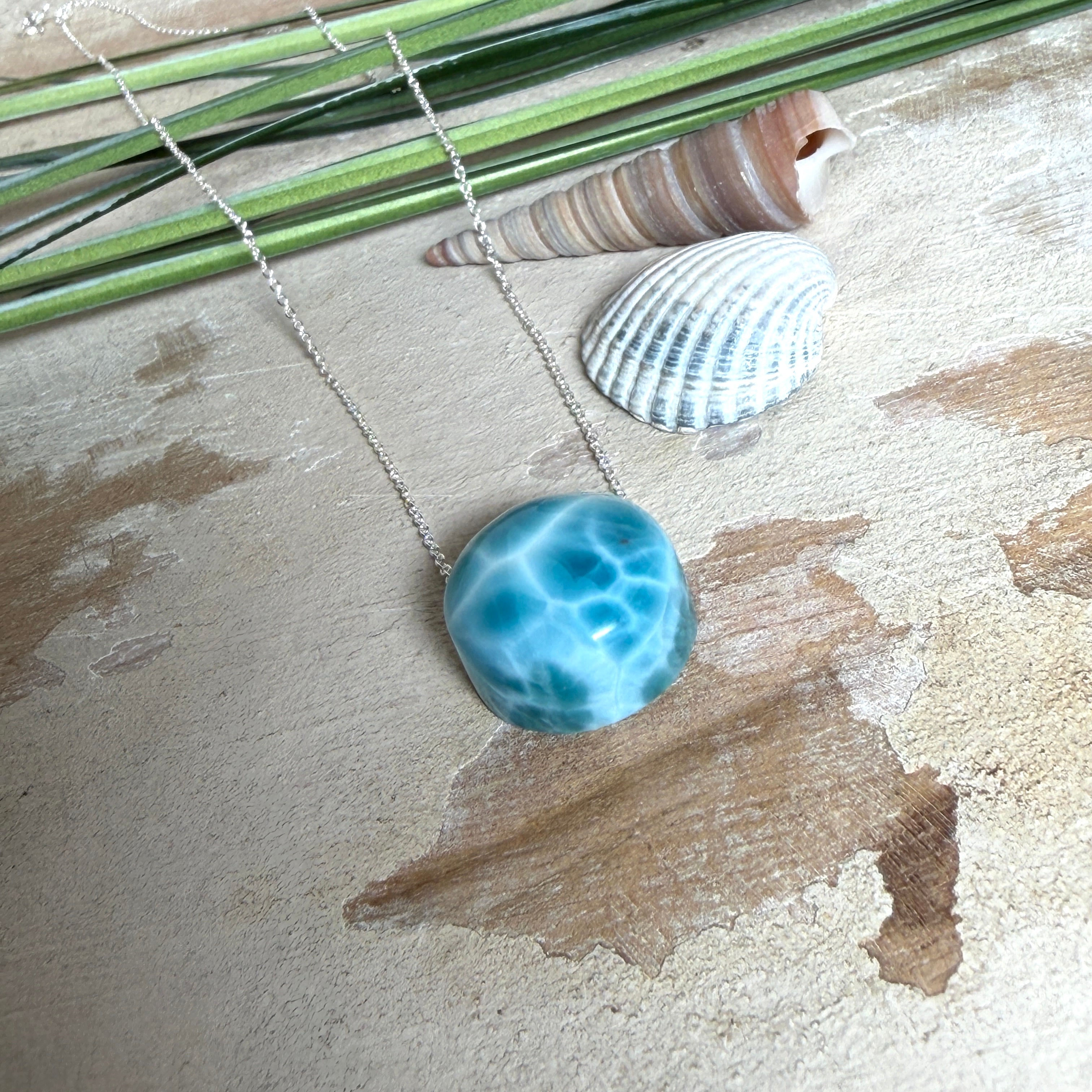 Feine Kette mit rundem Larimar-Cabochon in AA-Qualität. Der ca. 20 mm große Stein zeigt ein intensives Blau mit hellen, netzartigen Zeichnungen und ist mittig mit einer 2,5 mm Bohrung versehen, durch die eine zarte 925 Silberkette (45 cm, ca. 1 mm stark) geführt wird. 