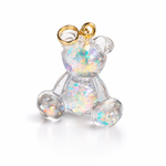 Kleiner Bärchen-Anhänger aus transparentem Harz mit irisierenden Flakes in Regenbogen-Schimmer, goldfarbene Anhängerschlaufe aus Edelstahl. Größe ca. 2,2 × 2,1 cm. Handgefertigtes Unikat; Flakes-Anordnung variiert, vereinzelt kleine Luftbläschen möglich.