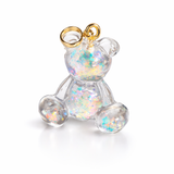 Kleiner Bärchen-Anhänger aus transparentem Harz mit irisierenden Flakes in Regenbogen-Schimmer, goldfarbene Anhängerschlaufe aus Edelstahl. Größe ca. 2,2 × 2,1 cm. Handgefertigtes Unikat; Flakes-Anordnung variiert, vereinzelt kleine Luftbläschen möglich.