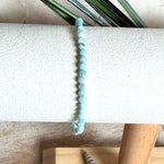 Zartes Larimar-Armband „Lagunenlicht“ mit facettierten 3 mm Perlen aus seltenem Atlantisstein auf Elastikfaden. Die kleinen Larimarsteine zeigen sanfte Blau- und Weißtöne wie Lagunenwasser. Innenumfang ca. 19 cm. Fotografiert auf Muscheln, einem dekorativen Stein und in einer schwarzen Schmuckbox von ZeitlosSchmuckDesign im maritimen Stil.
