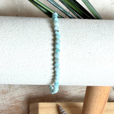 Zartes Larimar-Armband „Lagunenlicht“ mit facettierten 3 mm Perlen aus seltenem Atlantisstein auf Elastikfaden. Die kleinen Larimarsteine zeigen sanfte Blau- und Weißtöne wie Lagunenwasser. Innenumfang ca. 19 cm. Fotografiert auf Muscheln, einem dekorativen Stein und in einer schwarzen Schmuckbox von ZeitlosSchmuckDesign im maritimen Stil.
