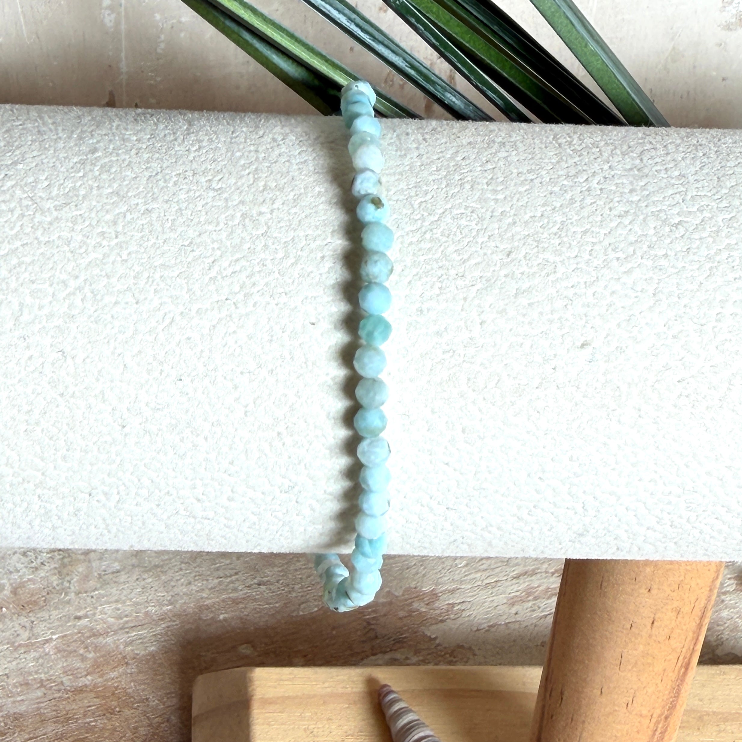 Zartes Larimar-Armband „Lagunenlicht“ mit facettierten 3 mm Perlen aus seltenem Atlantisstein auf Elastikfaden. Die kleinen Larimarsteine zeigen sanfte Blau- und Weißtöne wie Lagunenwasser. Innenumfang ca. 19 cm. Fotografiert auf Muscheln, einem dekorativen Stein und in einer schwarzen Schmuckbox von ZeitlosSchmuckDesign im maritimen Stil.
