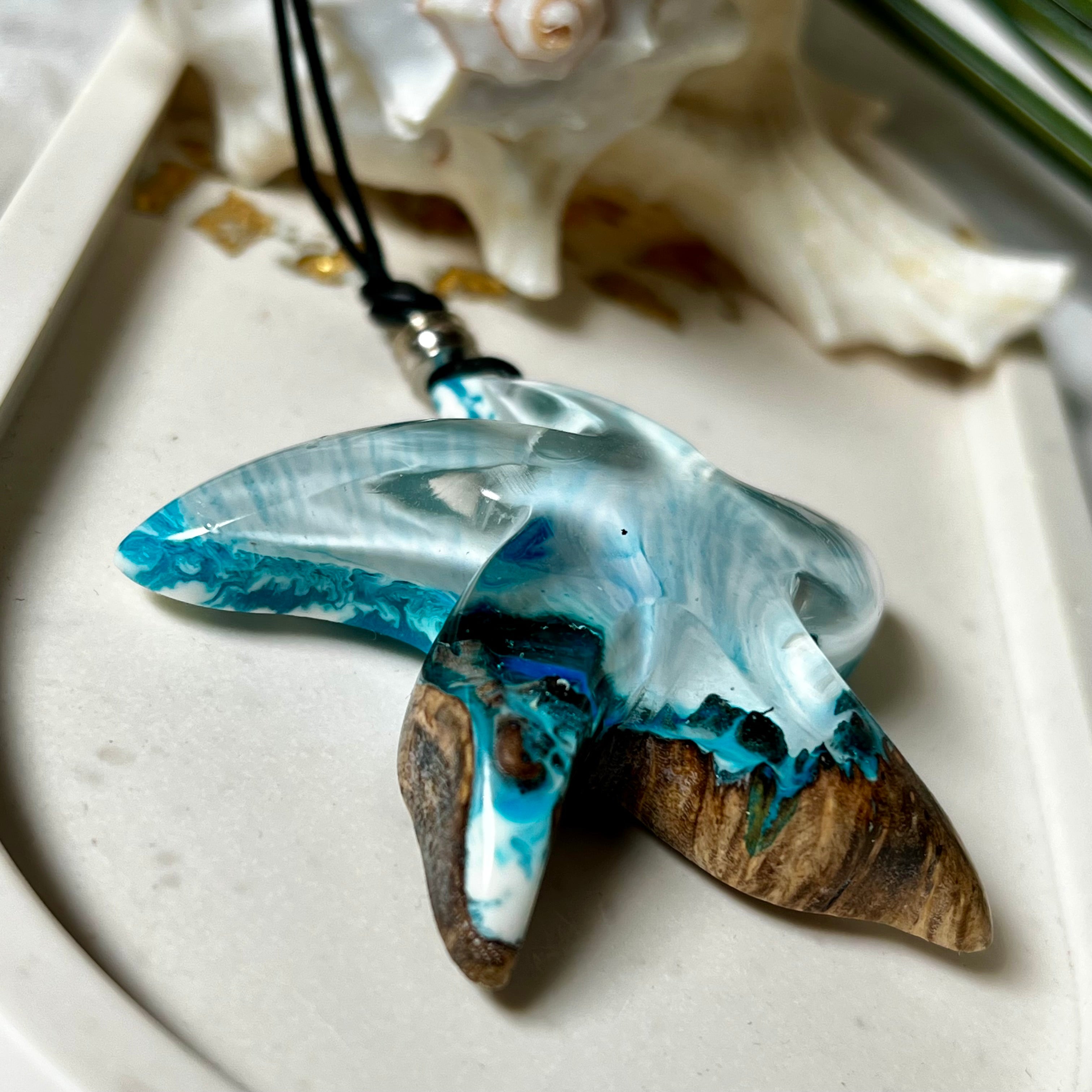 Handgefertigte Halskette in Seestern-Form mit Anhänger aus Naturholz und blau-weiß marmoriertem Epoxidharz. Das Schmuckstück ist einzigartig gestaltet und spiegelt maritimen Stil und Naturverbundenheit wider. Getragen an einem verstellbaren Lederband mit Holzperlen. Ideal für Meeresliebhaber und Naturfreunde.