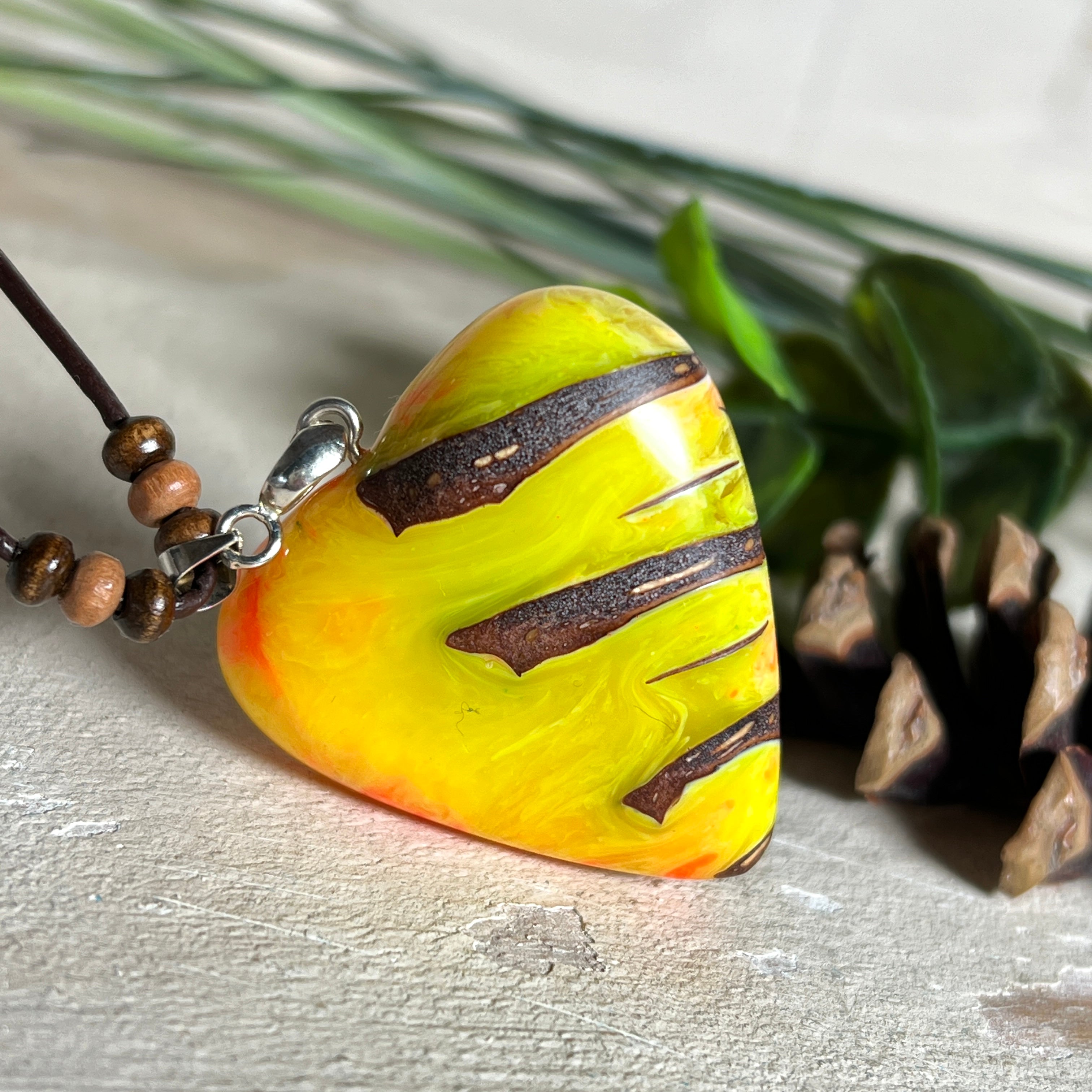 Herz-Anhänger aus Pinienzapfen & Harz, fluoreszierend bei Schwarzlicht. Farben Gelb-Orange-Weiß, Größe 4,2 × 3,8 cm. Lederband verstellbar.