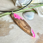 Handgefertigter Surfbrett-Anhänger „Pink Glow“ aus edlem Olivenholz und fluoreszierendem Epoxidharz in Pink & Weiß. Fluoreszierend bei Schwarzlicht, mit Edelstahl-Anhängerschlaufe und schwarzer Lederkette (45 cm + 5 cm Verlängerung). Ein maritimes Unikat – perfekt als Geschenk für Surfer und Meeresliebhaber.