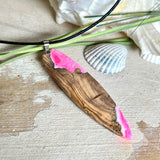 Handgefertigter Surfbrett-Anhänger „Pink Glow“ aus edlem Olivenholz und fluoreszierendem Epoxidharz in Pink & Weiß. Fluoreszierend bei Schwarzlicht, mit Edelstahl-Anhängerschlaufe und schwarzer Lederkette (45 cm + 5 cm Verlängerung). Ein maritimes Unikat – perfekt als Geschenk für Surfer und Meeresliebhaber.