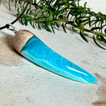 Handgefertigter Anhänger aus Edelholz und transparent-türkisblauem und weißen Epoxidharz, glatt poliert. Größe ca. 6,5 × 2,0 cm. Mit Edelstahlöse an schwarzer Lederkette (45 cm + 5 cm Edelstahl-Verlängerung, Karabiner). Moderner, unisex tragbarer Schmuck mit natürlicher Holzmaserung; kleine Lufteinschlüsse sind charakteristisch.