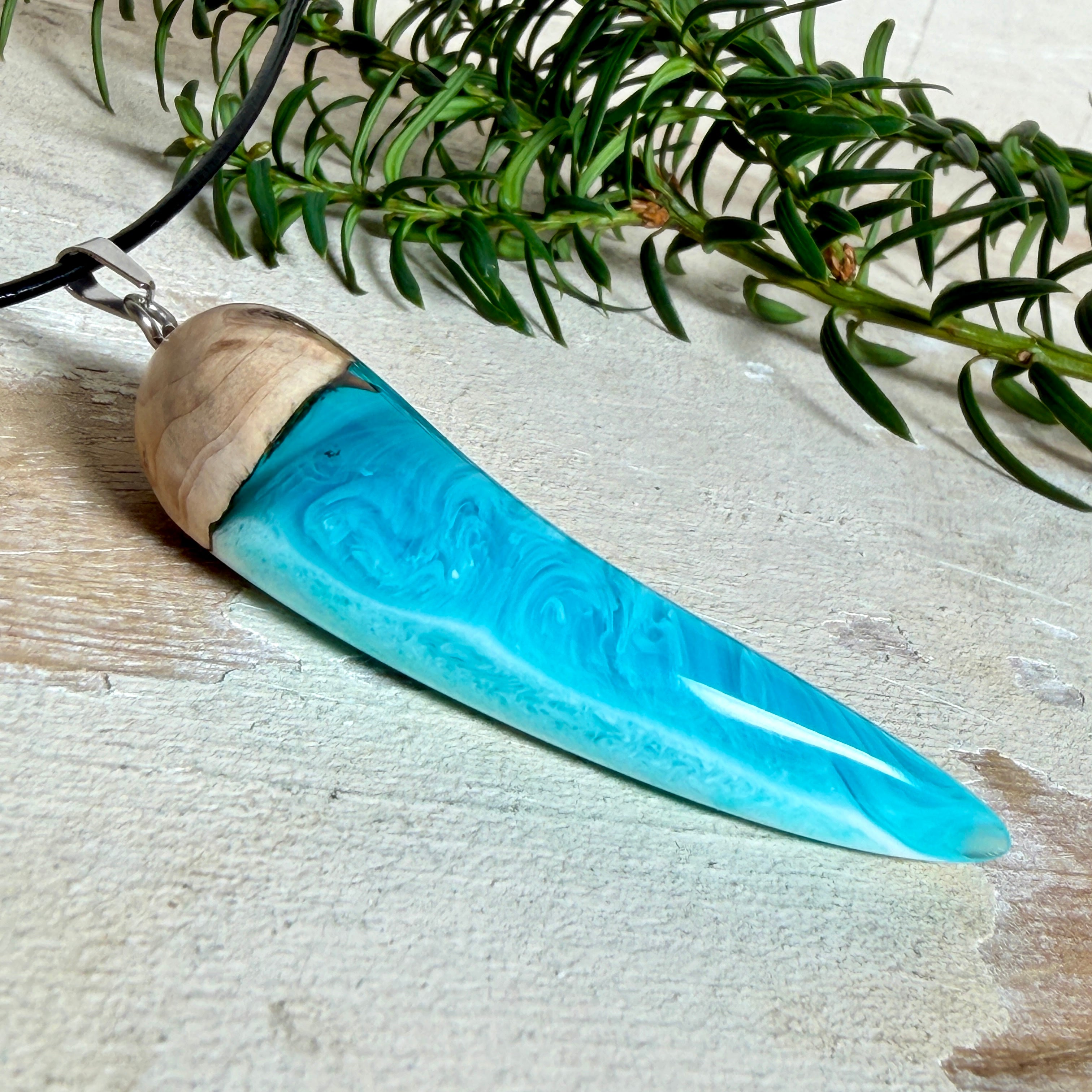 Handgefertigter Anhänger aus Edelholz und transparent-türkisblauem und weißen Epoxidharz, glatt poliert. Größe ca. 6,5 × 2,0 cm. Mit Edelstahlöse an schwarzer Lederkette (45 cm + 5 cm Edelstahl-Verlängerung, Karabiner). Moderner, unisex tragbarer Schmuck mit natürlicher Holzmaserung; kleine Lufteinschlüsse sind charakteristisch.