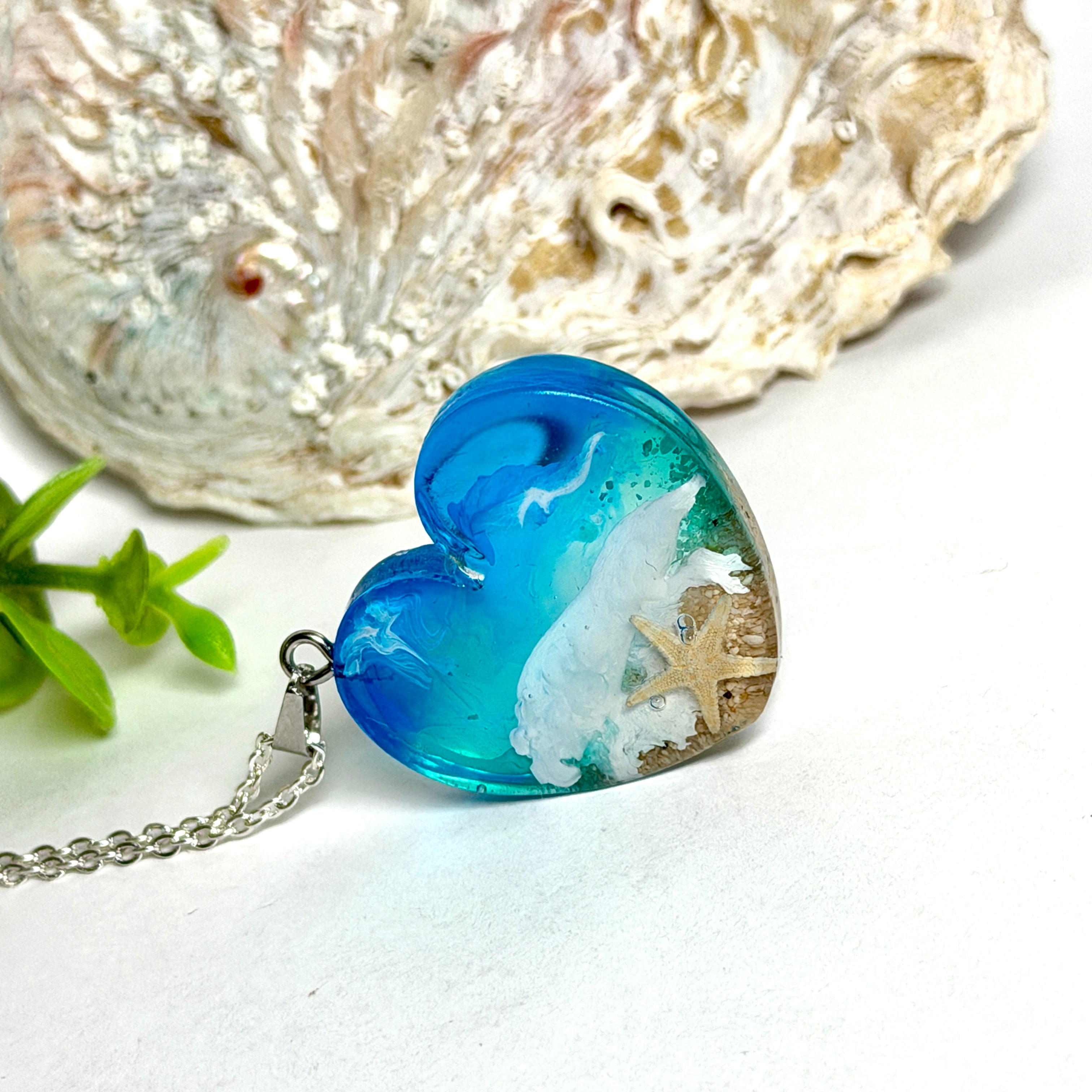 Ein herzförmiger Anhänger mit einer ganzen Ozeanwelt darin: Welle, Sand und Seestern in leuchtendem Blau und Türkis – handgegossen, einzigartig, unvergesslich. Mit versilberter Kette (46 cm) und Edelstahl-Karabiner.