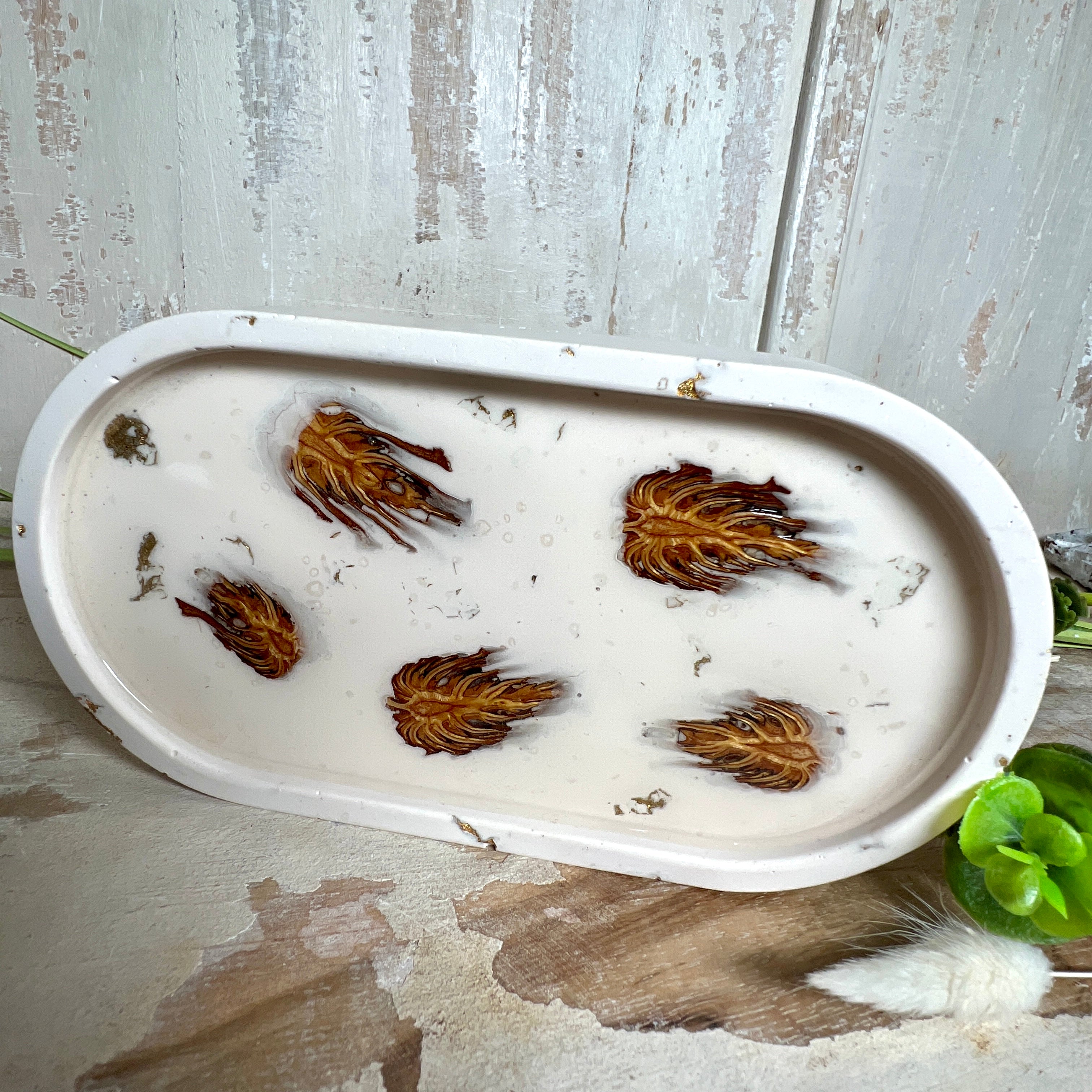 Handgefertigtes Schmucktablett aus Jesmonite mit echten Zapfen, die in einer glänzenden Resin-Schicht eingebettet sind. Die ovale Form und die natürliche Farbgebung machen es zu einem stilvollen Wohnaccessoire. Mit rutschfesten Korkpunkten auf der Unterseite ideal als Ablage für Schmuck, Schlüssel oder Dekoartikel. Jeder Artikel ist ein Unikat aus Handarbeit – Lieferung ohne Dekoration.