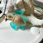 Handgefertigter Schildkröten-Anhänger Turtle Harmony aus echtem Meersand und transparent-türkisfarbenem Harz, kombiniert mit einer kleinen Jaspisperle. Symbol für Weisheit, Schutz und Harmonie. Mit Edelstahl-Anhängerschlaufe und Lederkette (45 + 5 cm). Maritimer Schmuck als Unikat, ideal als liebevolles Geschenk oder stilvolles Accessoire für den Alltag.