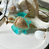 Handgefertigter Schildkröten-Anhänger Turtle Harmony aus echtem Meersand und transparent-türkisfarbenem Harz, kombiniert mit einer kleinen Jaspisperle. Symbol für Weisheit, Schutz und Harmonie. Mit Edelstahl-Anhängerschlaufe und Lederkette (45 + 5 cm). Maritimer Schmuck als Unikat, ideal als liebevolles Geschenk oder stilvolles Accessoire für den Alltag.