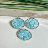 Runder Anhänger „Atlantis Dream“ aus antik-silberfarbener Zinklegierung, gefüllt mit kleinen Larimar-Edelsteinchen und klarem Resin. Die Larimarsteine zeigen sanfte Blau- und Weißtöne, die an das Meer erinnern. Durchmesser ca. 22 mm, handgefertigtes Unikat, fotografiert auf maritimem Untergrund mit kleinen Larimarsteinen und Muscheln zur Größenorientierung.