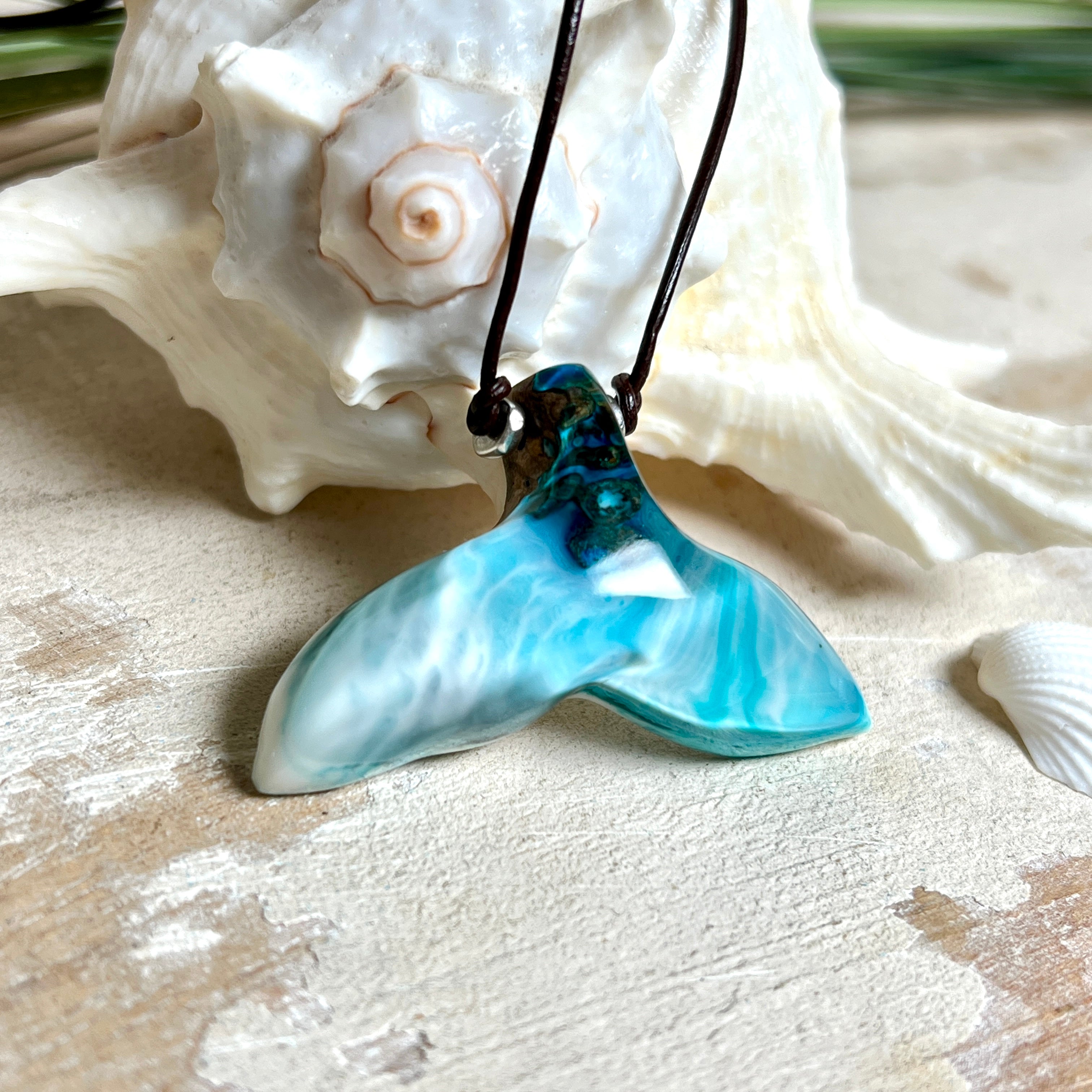 Walflossen-Anhänger „Flossenklang“ – handgefertigtes Unikat aus Maserholz und türkis-blau-grauen und weißem Harz. Die elegant geschwungene Form erinnert an die Flosse eines Wals und symbolisiert Freiheit, Stärke und Naturverbundenheit. Mit verstellbarem braunem Lederband gefertigt, ist jedes Stück ein individuelles Schmuckstück für Meeresliebhaber und Natursuchende. Maritimer Halsschmuck, inspiriert vom Ozean, glatt poliert und mit Liebe zum Detail von Hand gearbeitet.