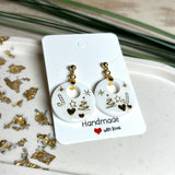 Handgefertigte Ohrringe aus weißem und klarem Harz mit goldenen Weihnachtsmotiven – Sterne, Herzen, Tannenbaum und Zuckerstange. Ohrstecker aus 925 Silber vergoldet, Anhängerschlaufe vergoldet. Größe ca. 37 mm × 25 mm. Leichte, elegante Festtagsohrringe mit warmem Goldglanz und winterlicher Ausstrahlung.
