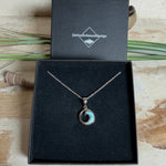 Feine Wellen-Kette aus rhodiniertem 925 Silber. Der runde Anhänger zeigt eine stilisierte Welle mit hellblauem Larimar-Cabochon, eingefasst in poliertem Silber. Größe des Anhängers ca. 23 x 13 mm, an einer 45 cm langen, 1 mm starken, rhodinierten Silberkette. 