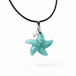 Seestern-Anhänger aus transparentem Harz mit echtem Meersand ( leicht eingefärbt), in blautürkis Strand-Look, mit kleiner Süßwasserperle als Anhänger-Detail. Edelstahlöse, schwarze Lederkette mit Edelstahl-Karabiner und Verlängerung (45 cm + 5 cm). Anhänger ca. 3,5 × 3,5 cm. Handgefertigtes Unikat; vereinzelt kleine Luftbläschen möglich, typisch für Handarbeit.