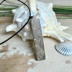 Rechteckiger Stabanhänger aus Maserholz und glasklarem Epoxidharz in tiefen Blau- und Türkistönen mit organischer Lagunen/Riff-Optik. Hochglanzpoliert, ca. 5,3 × 1,2 cm. Der Anhänger hängt an einer schwarzen Lederkette mit Edelstahl-Karabiner und 5-cm-Verlängerung (45 + 5 cm); die Anhängerschlaufe ist ebenfalls aus Edelstahl. Handgefertigtes Unikat, Lieferung in edler Schmuckbox – maritimer Look.