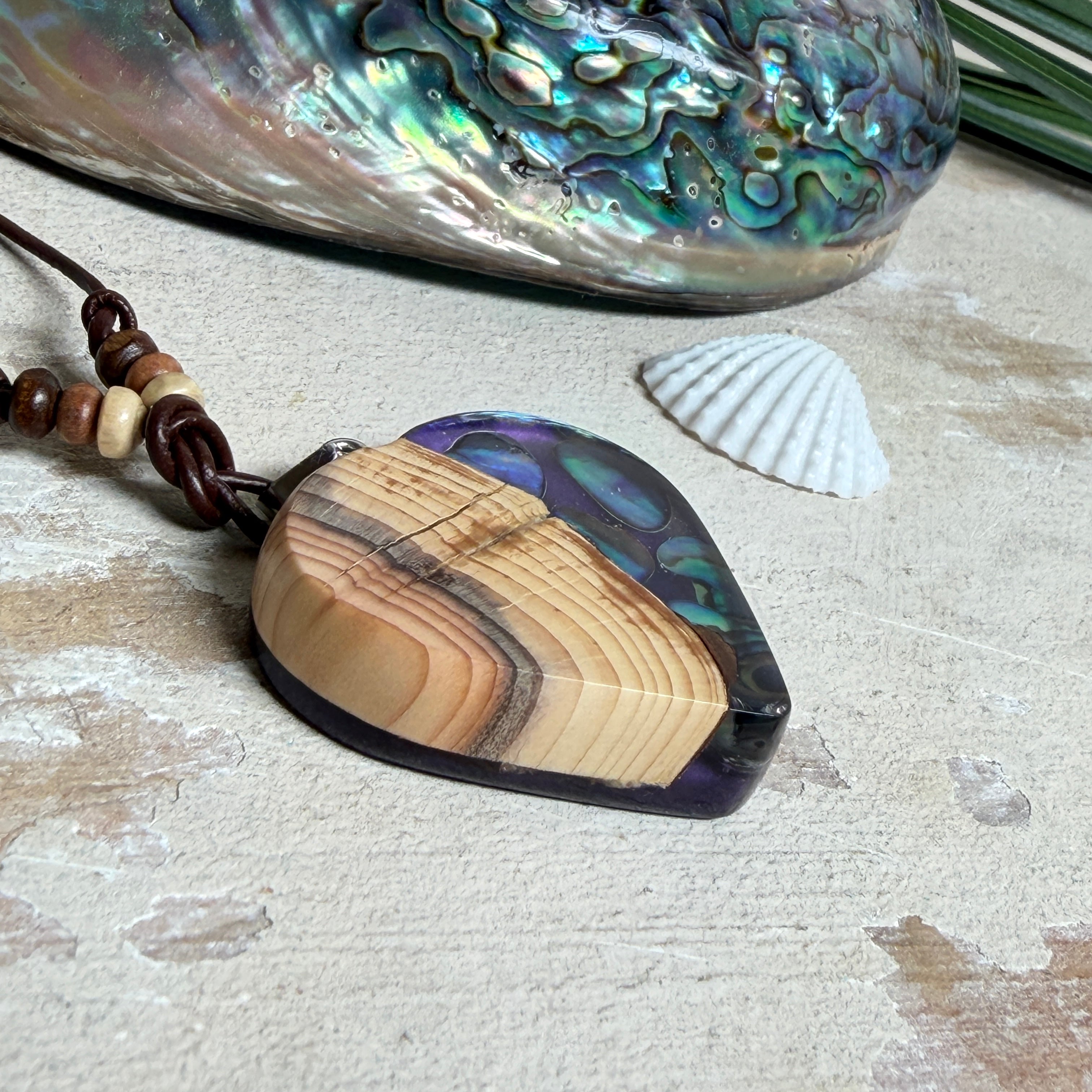 Handgemachter Herzanhänger aus Eibenholz mit lila Harz und Paua-Muschel-Inlay an braunem, verstellbarem Lederband.