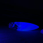 Surfbrett-Anhänger aus Maserholz und blau-weißem Epoxidharz, hochglanzpoliert, ca. 6,5 × 2 cm. An schwarzer Lederkette mit Edelstahl-Karabiner und 5-cm-Verlängerung; Edelstahl-Öse. Im Tageslicht lagunenblau, unter Schwarzlicht fluoreszierend – ideal als Party-/Festival-Schmuck. Handgefertigtes Unikat, Lieferung in edler Schmuckbox.