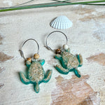 Türkisfarbene Schildkröten-Creolen an feinen 16-mm-Ringen aus 925 Silber, jeweils mit echtem Strandsand im Harz eingebettet und mit kleinen Jaspis-Edelsteinperlen verziert; handgefertigtes Unikat mit sommerlich-maritimem Look, fotografiert als Freisteller, Nahaufnahme oder auf dekorativem Untergrund.