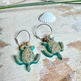 Türkisfarbene Schildkröten-Creolen an feinen 16-mm-Ringen aus 925 Silber, jeweils mit echtem Strandsand im Harz eingebettet und mit kleinen Jaspis-Edelsteinperlen verziert; handgefertigtes Unikat mit sommerlich-maritimem Look, fotografiert als Freisteller, Nahaufnahme oder auf dekorativem Untergrund.