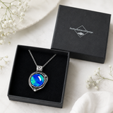 Labor-Opal-Anhänger „Galactic Glow“ in Antik-Silber-Optik mit blau-grün schimmerndem Cabochon liegt in einer geöffneten schwarzen Schmuckbox von ZeitlosSchmuckDesign.