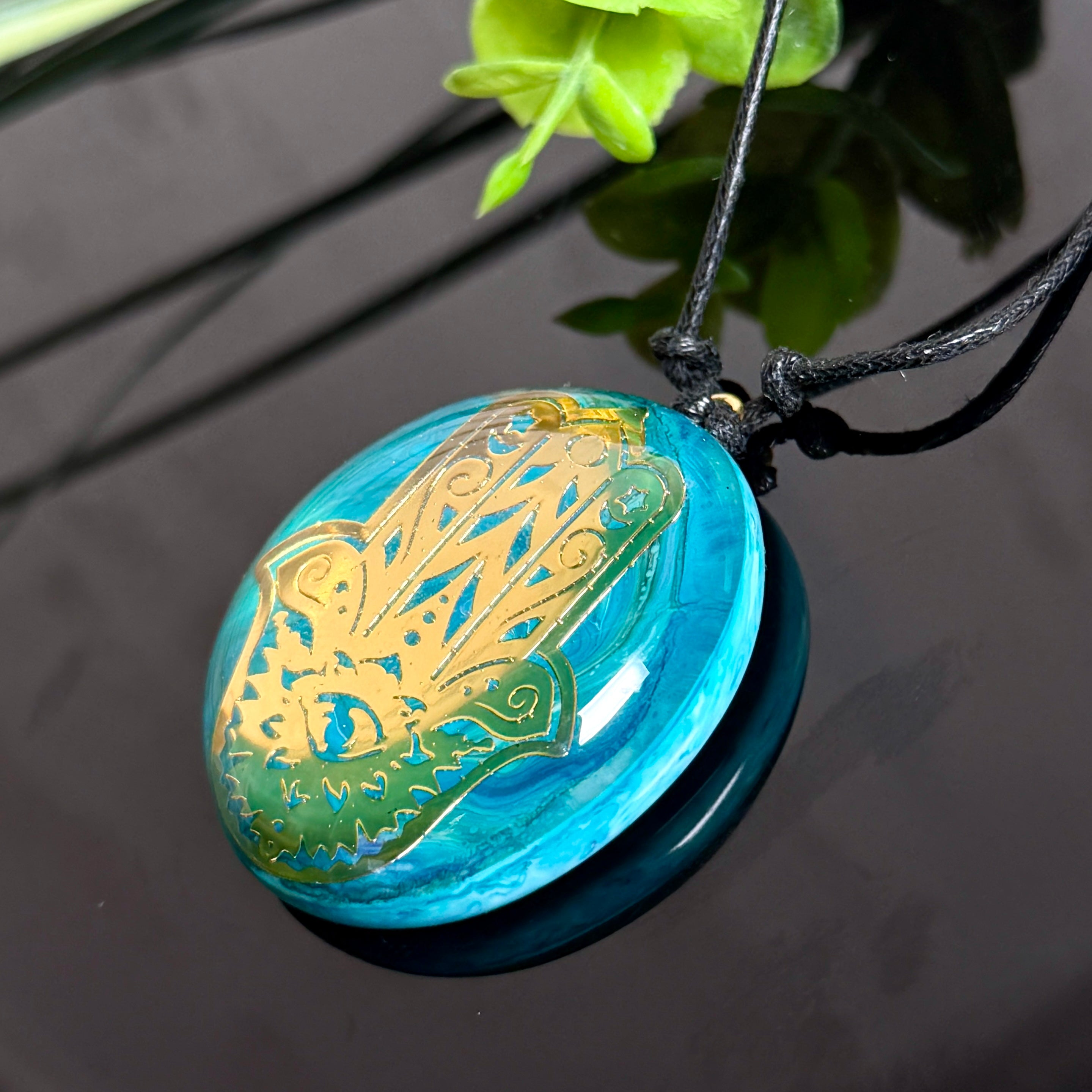 Hamsa Hand Halskette türkis – rundes Epoxidharz-Cabochon mit goldener Hamsa, an schwarzem Baumwollband mit Schiebeknoten