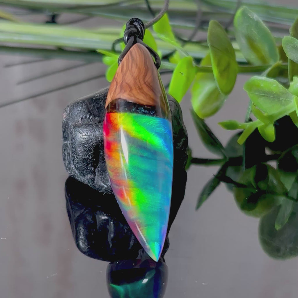 Der handgefertigte Anhänger „Celestial Flame“ kombiniert warmes Olivenholz mit glasklarem Harz und irisierendem Opal. Das einzigartige Farbspiel erinnert an Polarlichter und verleiht dem Schmuckstück eine mystische Tiefe. Die Oberfläche ist glatt poliert, der Anhänger wird an einem verstellbaren Lederband getragen – ein ausdrucksstarkes Unikat für alle, die Naturmaterialien und kreative Farben lieben.